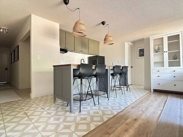 Une cuisine moderne dotée d’un îlot central, de tabourets de bar, de luminaires suspendus et d’un revêtement de sol à motifs.