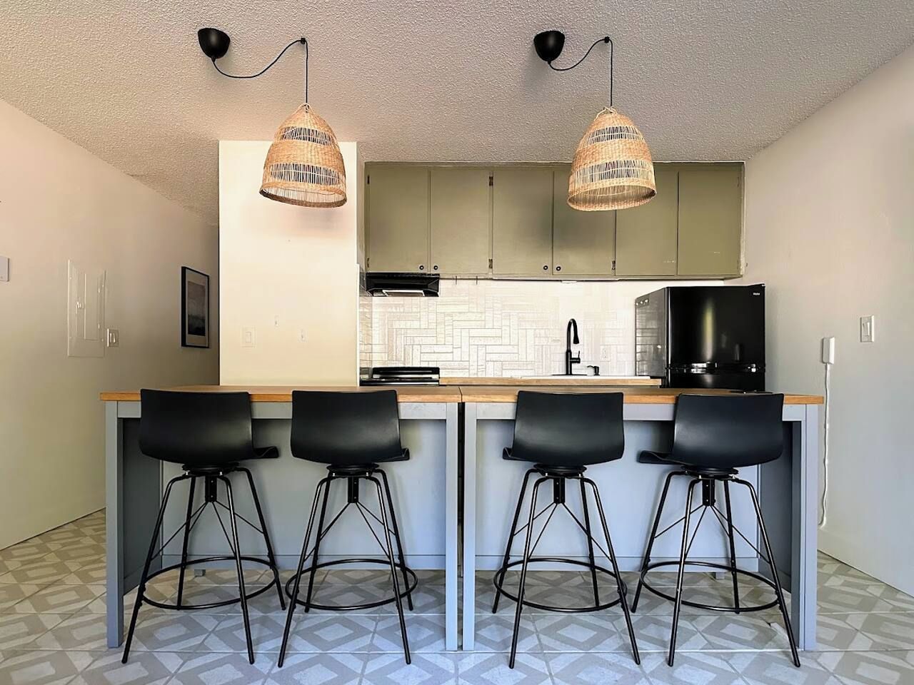 Una cocina con una isla central, taburetes de bar, luces colgantes y un microondas.