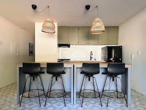 A kitchen with a central island, bar stools, pendant lights, and a microwave.