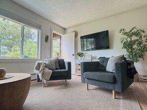 A living room with two sofas, a TV, a plant, and a window with a view of trees. - Resting Beach Place | Luxurious Beachfront Condo (Neskowin)
