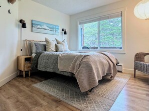 Une chambre à coucher avec un lit, des tables de chevet, une fenêtre donnant sur des arbres et un fauteuil.