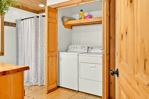 Ein Waschraum mit einem Holzkabinet, einer Waschmaschine und einem Regal mit Reinigungsmitteln.