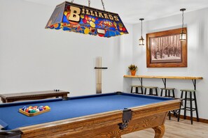 Ein Billardraum mit Pooltisch, Hockern, einer Billardständerung und einem hängenden Schild.