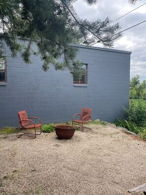 A building with a grey exterior, two red chairs, and a large planter in the foreground. - The Yellow House (Lake Mills)