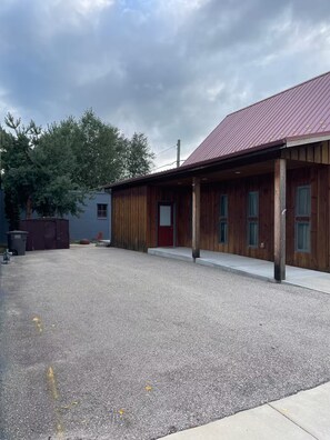 Ein Gebäude mit rotem Dach und Holzverkleidung, einer Schotterauffahrt und einem Baum im Hintergrund.