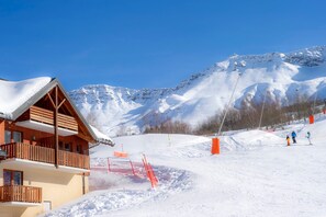 A wooden chalet with a balcony, a ski slope with orange barriers, and a mountain backdrop. - Au pied des pistes | Station animée et sportive (Saint-François-Longchamp)