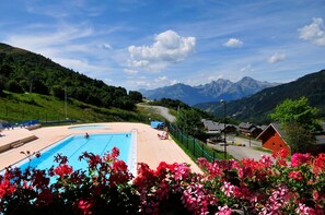 A swimming pool with a view of mountains, surrounded by greenery and a few buildings. - Au pied des pistes | Station animée et sportive (Saint-François-Longchamp)