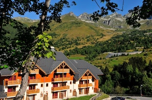 A chalet-style hotel with multiple balconies, set against a mountainous backdrop. - Ski aux pieds | Commerces à proximité | Balcon (Saint-François-Longchamp)