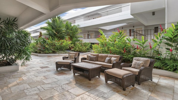 A spacious outdoor lounge area with wicker furniture, potted plants, and a view of the building's interior.