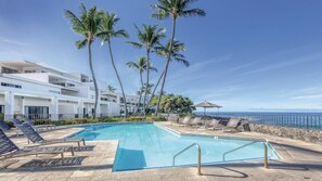 A pool area with lounge chairs and palm trees, overlooking a body of water.