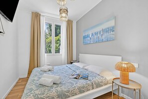 A modern bedroom with a large bed, a side table, a lamp, and a painting on the wall. - Kamy Home | Steps to the Lake & Free Park, Gardone Riviera, Italy (Gardone Riviera)
