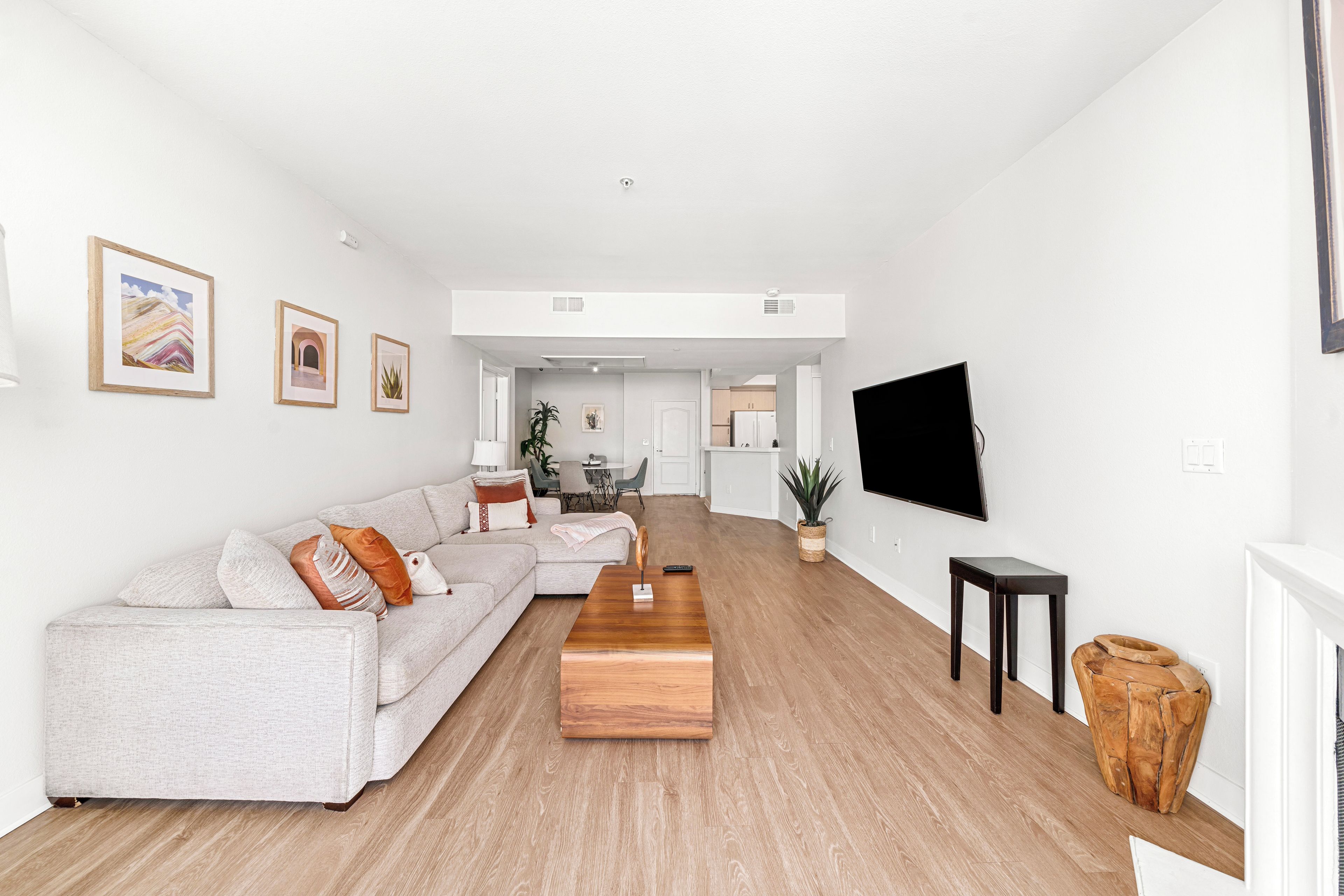 A modern living room with a sectional sofa, a wooden coffee table, and a flat-screen TV mounted on the wall.