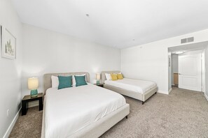 A hotel room with two beds, a nightstand with a lamp, and a door leading to another room.