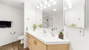 Un bagno moderno con un lavandino bianco, mobili in legno, uno specchio grande e una cabina doccia in vetro.