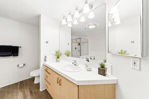 Un bany modern amb un lavabo blanc, armaris de fusta, un mirall gran i una cabina de dutxa de vidre.