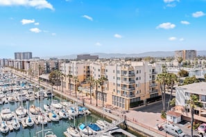 A marina with numerous boats docked, surrounded by multi-story buildings with balconies and palm trees.