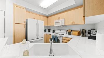 A modern kitchen with white cabinets, a stainless steel refrigerator, a microwave, and a stove.
