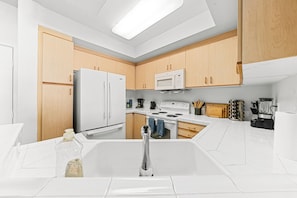 A modern kitchen with white cabinets, a stainless steel refrigerator, a microwave, and a stove.