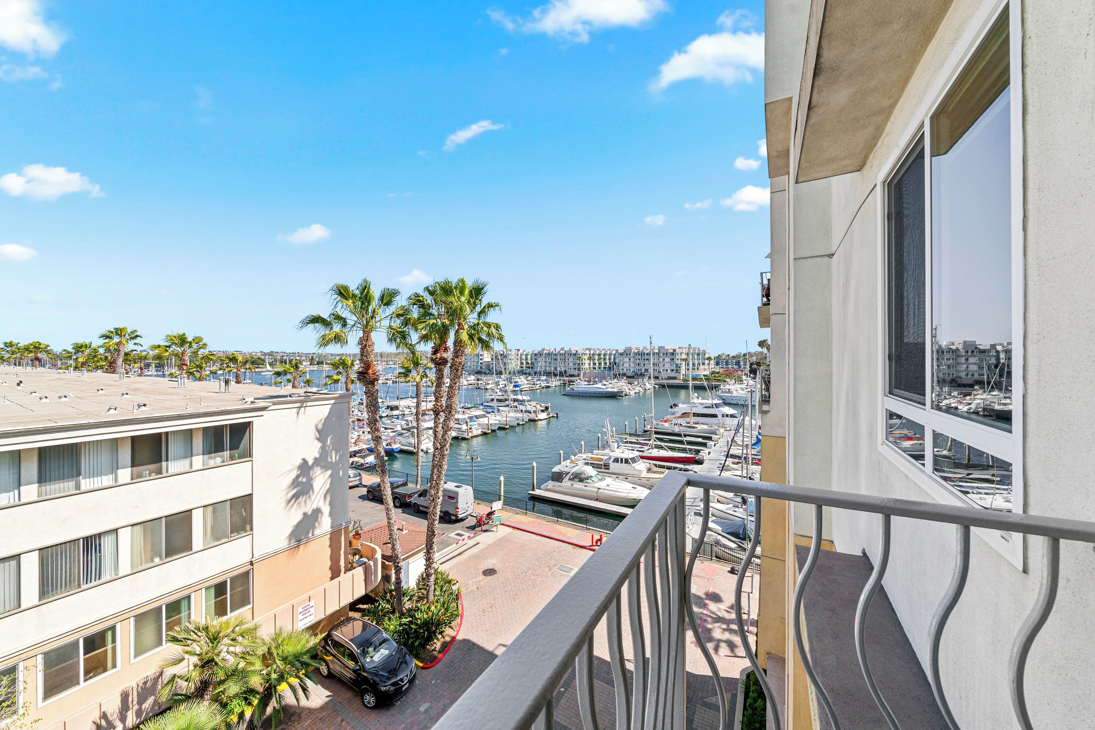 A balcony with a view of a marina, palm trees, and a building with multiple windows.
