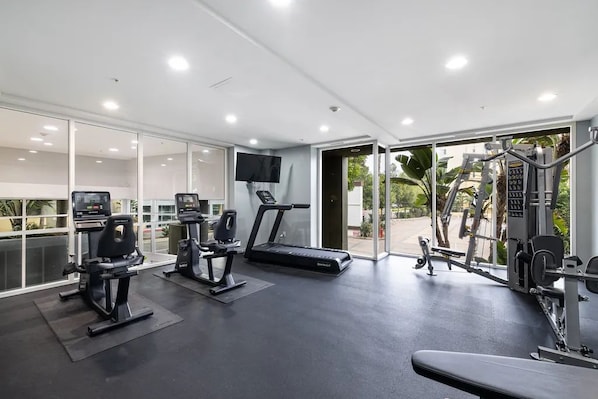 A modern gym with cardio machines, weightlifting equipment, and a TV screen.