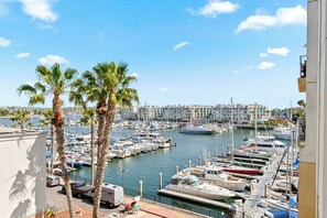 Un port de plaisance avec des bateaux amarrés, des palmiers et une vue sur la ville en arrière-plan.
