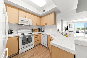 A modern kitchen with wooden cabinets, white appliances, and a large window providing a view of the outdoors.