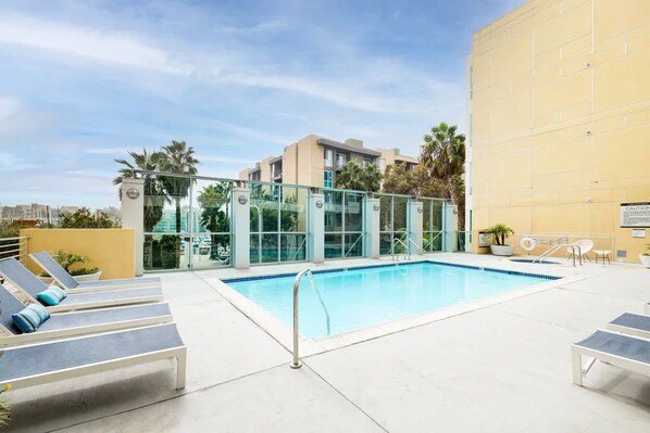An outdoor swimming pool with lounge chairs, a glass-enclosed building, and palm trees.