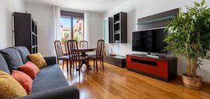 A modern living room with a sofa, dining table, chairs, a TV, and a potted plant.