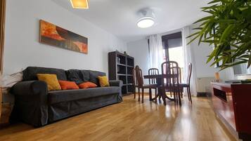 A living room with a sofa, chairs, a table, a bookshelf, and a painting on the wall.