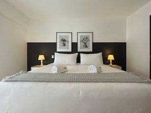 A hotel room with a large bed, two bedside lamps, a headboard with framed pictures, and neatly folded towels. - Barranco Sailor Apartment By Geko (Barranco)