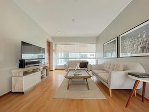 A modern living room with a flat-screen TV, a sofa, a coffee table, and a large window offering a view. - Barranco Sailor Apartment By Geko (Barranco)