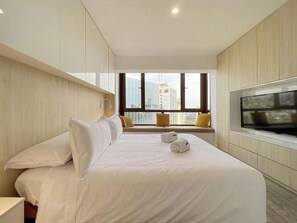 Ein Hotelzimmer mit einem großen Bett, einem Fernseher und einem Fenster mit Blick auf die Stadt.