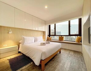 Ein modernes Schlafzimmer mit einem großen Bett, eingebauten Schränken, Nachttischlampen und einem Fenster mit Blick auf die Stadt.