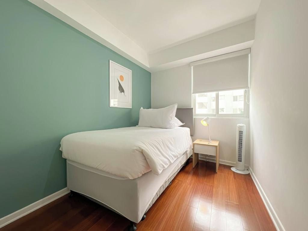 A bedroom with a bed, a bedside table, a lamp, and a window.