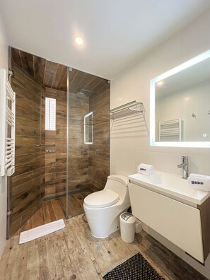 Ein Badezimmer mit einer Duschkabine aus Holz, einer Toilette, einem Waschbecken mit Spiegel und einem Handtuchhalter.