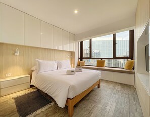 Ein modernes Schlafzimmer mit einem großen Bett, Einbauschränken, Nachttischlampen und einem Fenster mit Blick auf die Stadt.