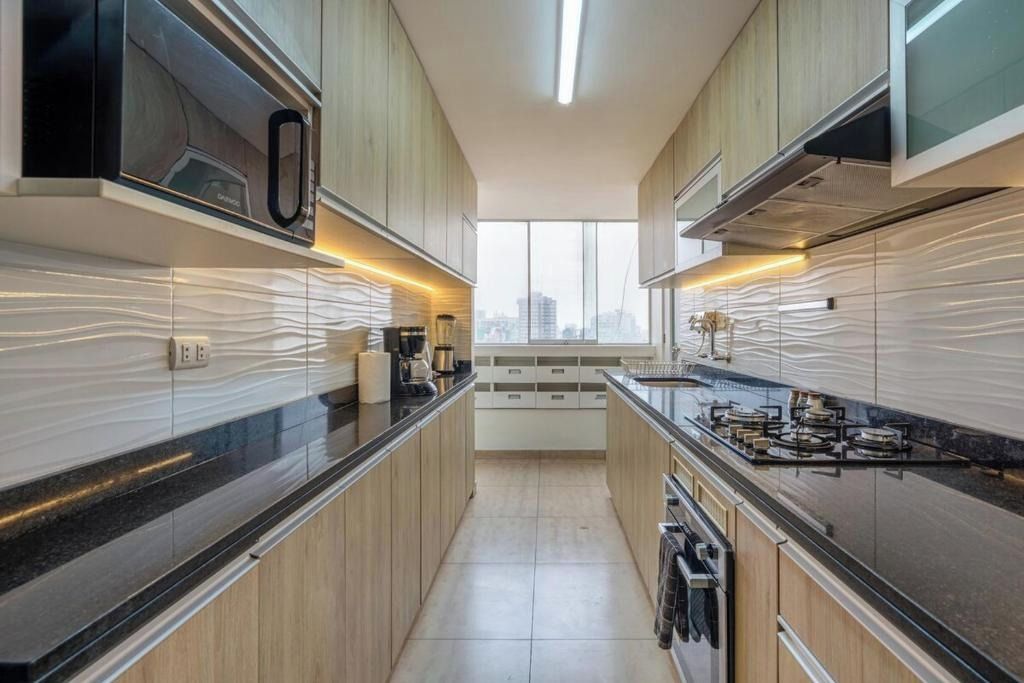 A modern kitchen with wooden cabinets, a black countertop, and a city view through the window.