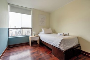 A bedroom with a bed, a nightstand, a window, and a wall-mounted artwork. - Contemporary Pardo Miraflores Apartment By Geko (Miraflores)