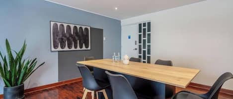 Ein Konferenzraum mit Holztisch, schwarzen Stühlen, einer Zimmerpflanze und einem an der Wand befestigten Kunstwerk.