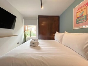 A hotel room with a bed, a TV mounted on the wall, a window with a view, and a door. - Modern Dalias Miraflores Apartment By Geko (Miraflores)
