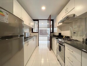 Una cocina moderna con electrodomésticos de acero inoxidable, armarios blancos y piso de baldosas.