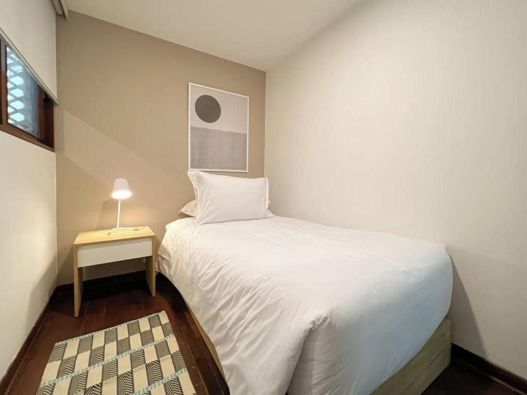 Un dormitorio con una cama individual, una mesita de noche, una lámpara y una obra de arte colgada en la pared.