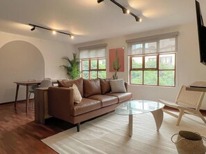 A modern living room with a leather sofa, a glass coffee table, and a dining area with a table and chairs. - Modern Dalias Miraflores Apartment By Geko (Miraflores)