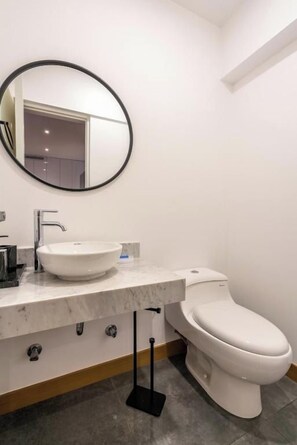 A modern bathroom with a white sink, a round mirror, and a toilet. - José Gonzales 626 Apartments Near Kennedy Park By Geko (Miraflores)