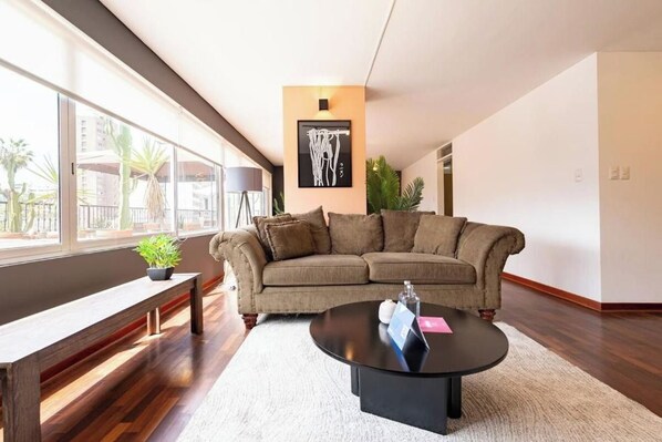 A modern living room with a sofa, a coffee table, and a bench. There is a framed artwork on the wall and a potted plant on the bench. - Urban Schell Miraflores Apartment By Geko (Miraflores)