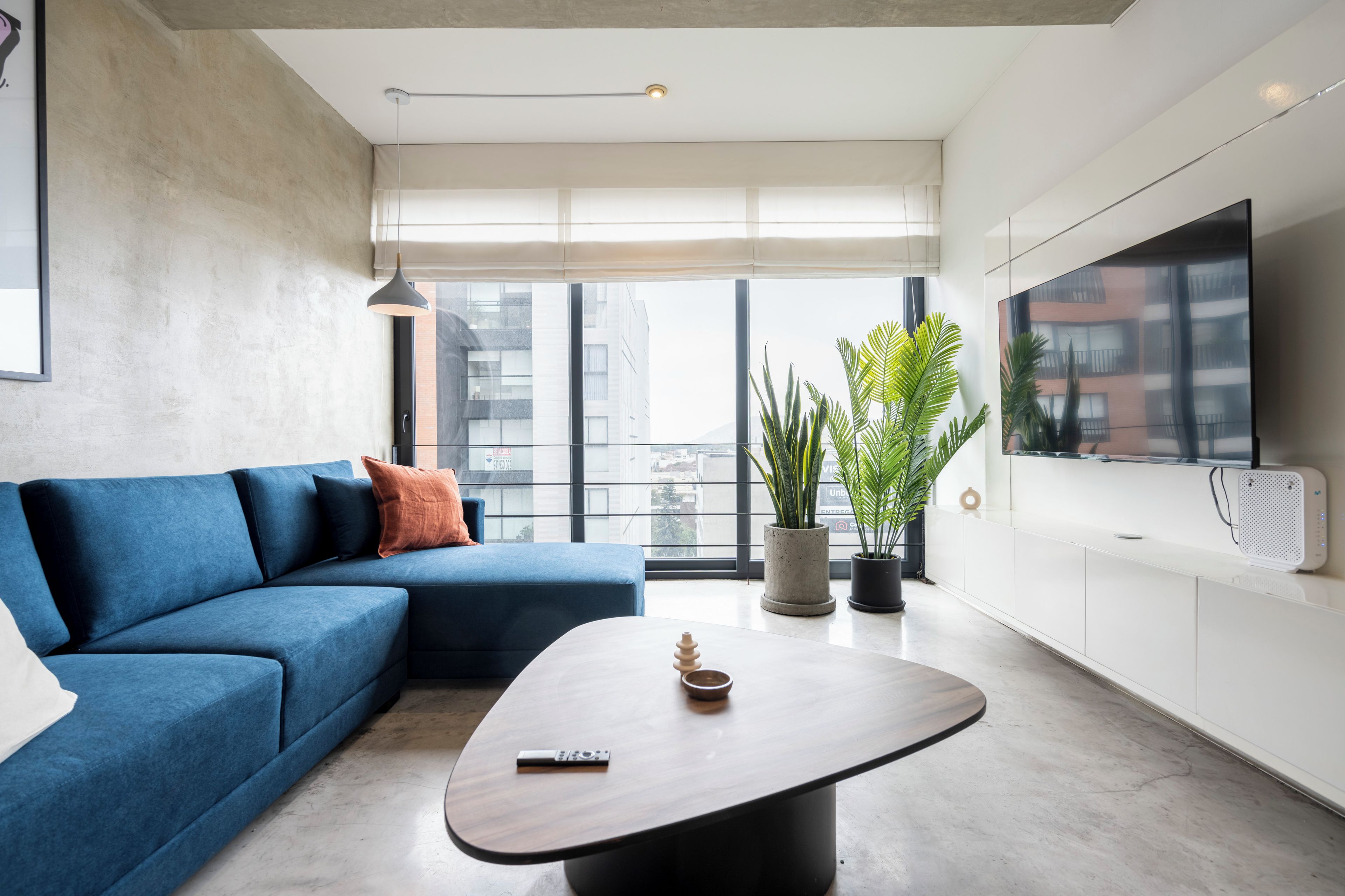 A modern living room with a blue sofa, a wooden coffee table, and a large window with a city view.