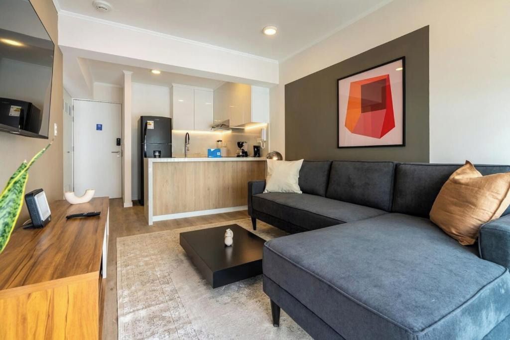 A modern living room with a grey sofa, a coffee table, and a kitchen area in the background.