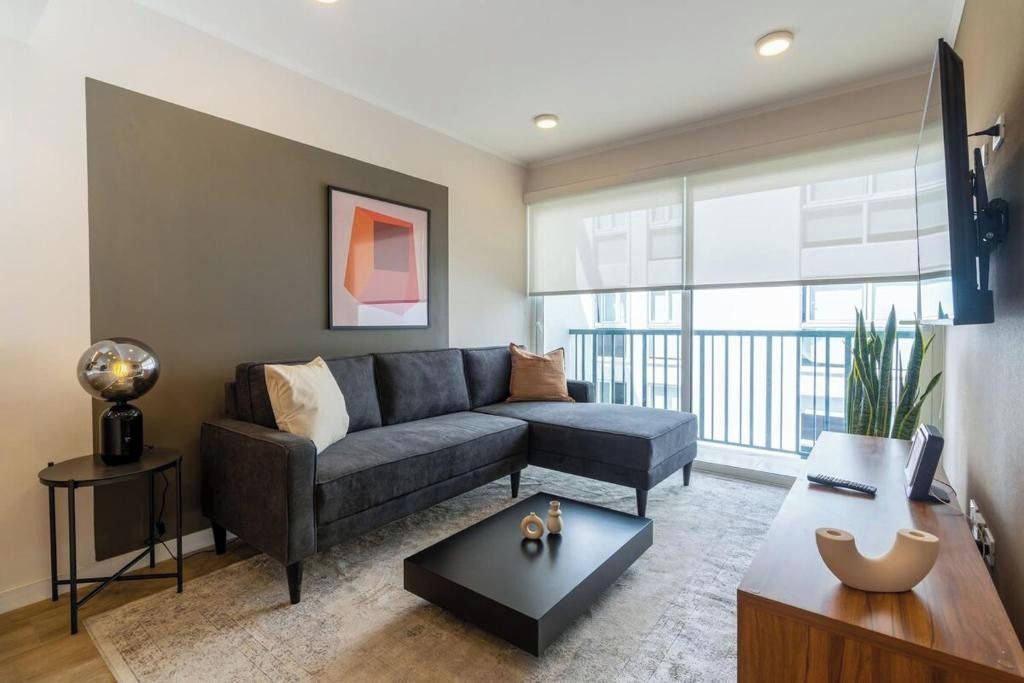 A modern living room with a sectional sofa, a coffee table, a side table with a lamp, and a large window with a view.
