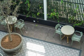 Eine Terrasse mit einem runden Tisch und Stühlen, einem Blumentopf und einem gemusterten Boden.