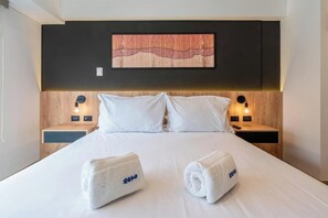 Ein Hotelzimmer mit einem Bett, zwei Nachttischen, einem Wandbild und zwei Handtüchern mit einem Logo.
